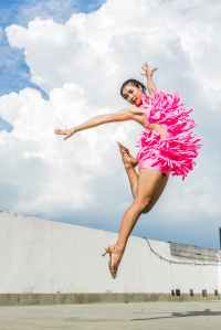 woman in pink dress doing jump shot while extending arms under white clouds